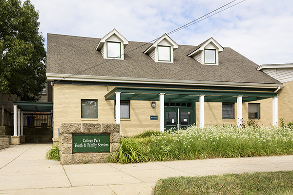 Exterior photo of a tan brick building with green trim and 3 dormer windows. A sign out front reads College Park Youth & Family Services.